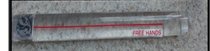 lupa de régua no formato retangular, comprida, sem cor/transparente, com um traço vermelho bem no meio que permite que o estudante com baixa visão tenha uma ampliação do texto em que está passando a lupa.